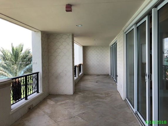View from a covered balcony with glass doors and railing, overlooking greenery.