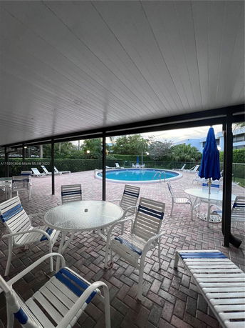 View of a circular swimming pool surrounded by patio furniture and a covered seating area.