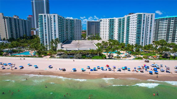 High-rise residential buildings facing a beach with umbrellas and people along the shore.