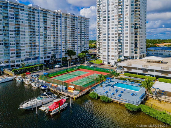 Aerial view of high-rise buildings with adjacent tennis courts and swimming pool along the waterfront.