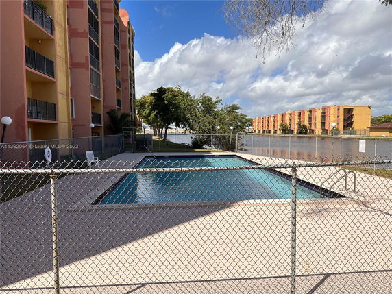 Swimming pool area next to an apartment building with a fenced perimeter.