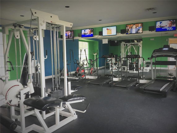 Interior view of a gym with exercise equipment and multiple TV screens.