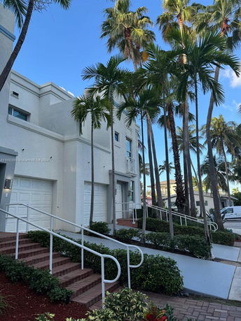 Front view of a multi-story house with a garage and surrounding palm trees.