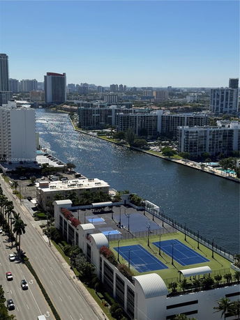 View of tall buildings and waterways from a high vantage point, showing a complex with rooftop tennis courts.