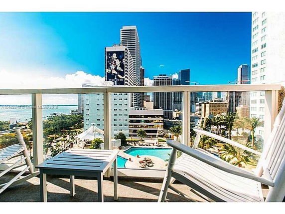 View from building showing a cityscape with high-rise buildings, a pool area, and a balcony with chairs and a table.