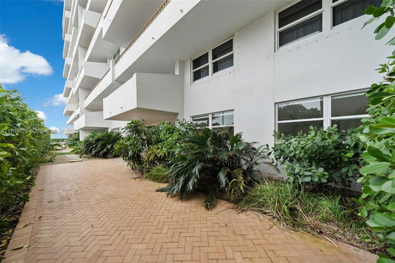 Side view of a multi-story building with large windows and a paved walkway lined with greenery.
