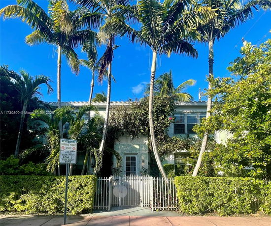 Front view of a two-story house with a gated entrance and surrounding palm trees.