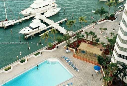 View from a high-rise building showing a swimming pool, marina with yachts, and a landscaped area.