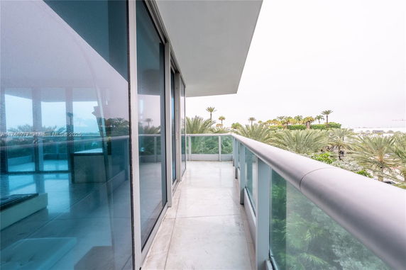 Balcony view with glass railing overlooking palm trees.