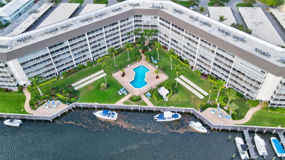 Aerial view of a waterfront building complex with a central swimming pool and surrounding green lawn.