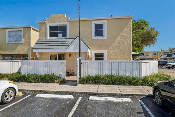Front view of a two-story house with a white fence and driveway parking.