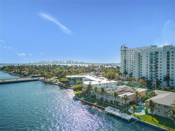 Aerial view of waterfront buildings with a surrounding water body and city skyline in the distance.