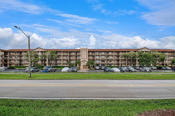 Front view of a multi-story residential building with balconies and a parking area.