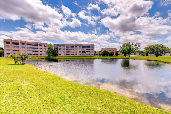 View of a multi-story building near a pond with green grassy surroundings.
