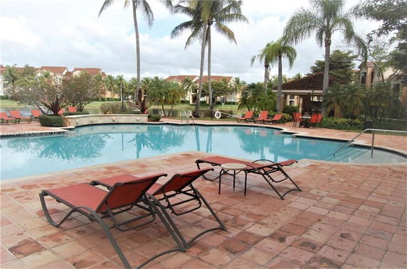 Outdoor swimming pool with lounge chairs and palm trees.