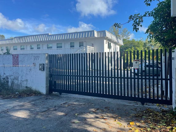 Front view of a white two-story building with a metal roof and gated entrance.