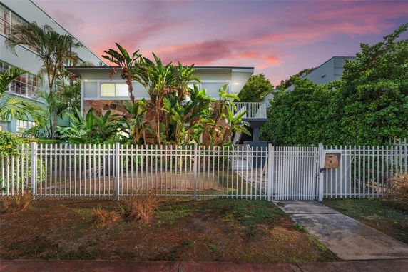 Front view of a modern house with a metal fence and tropical plants.