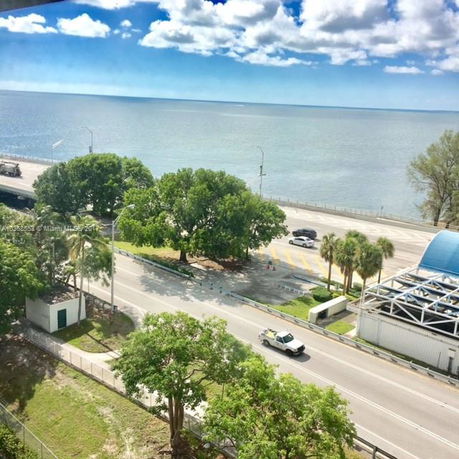 View from a building showcasing a road, trees, and a vast body of water extending into the horizon.
