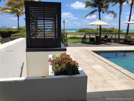 Outdoor area with a swimming pool and patio seating overlooking a beach.