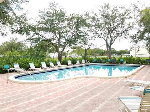 Outdoor swimming pool area with surrounding lounge chairs and trees.