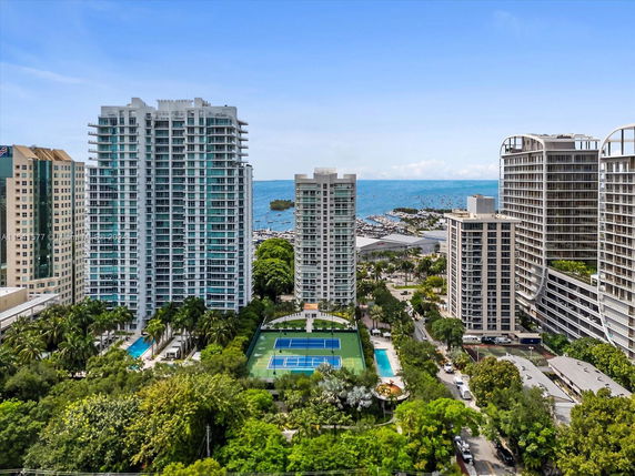 View of multiple high-rise buildings with a pool and tennis courts, and an ocean in the background.