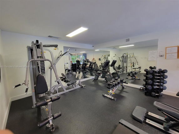 Indoor gym area with various exercise equipment and mirrors on the wall.