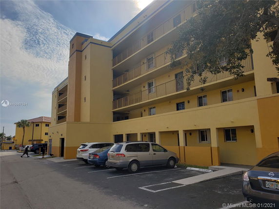 View of a multi-story apartment building with cars parked in front.