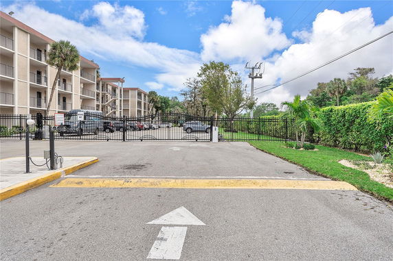 Outdoor parking area in front of a multi-story residential building with a gated entrance.