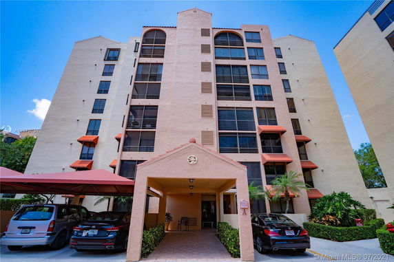 Front view of a multi-story apartment building with a covered entrance and parking area.