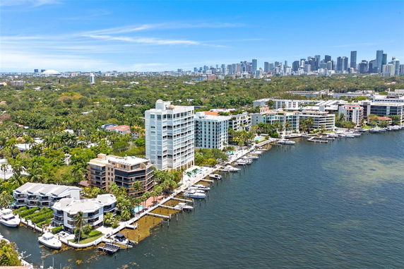 Aerial view of waterfront residential buildings with boats docked along the shoreline and a city skyline in the background.