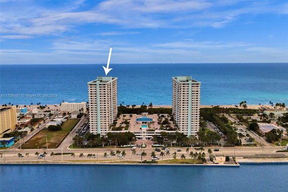 Aerial view of two tall residential buildings near the ocean, highlighting one building with an arrow.