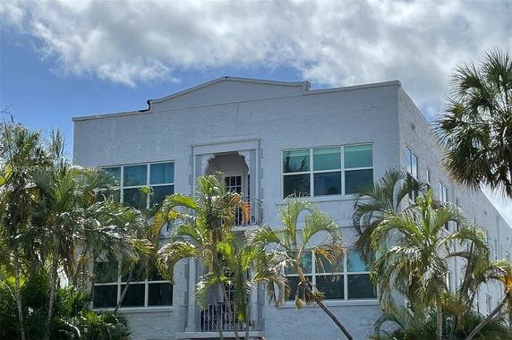 Front view of a multi-story building with large windows and tropical plants.