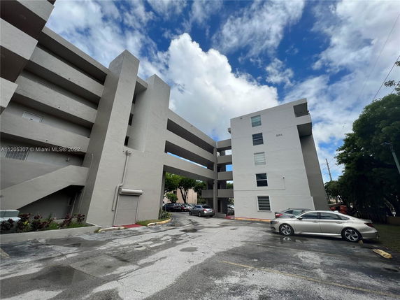 Front view of a multi-story apartment building with parking area visible in the foreground.