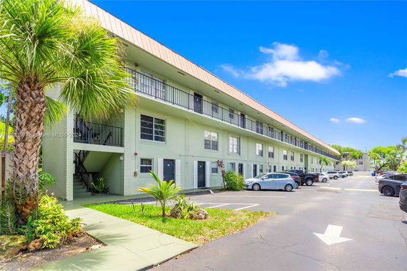Front view of a three-story residential building with a parking area in front.