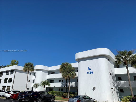 Front view of a multi-story white building with palm trees and parked cars.