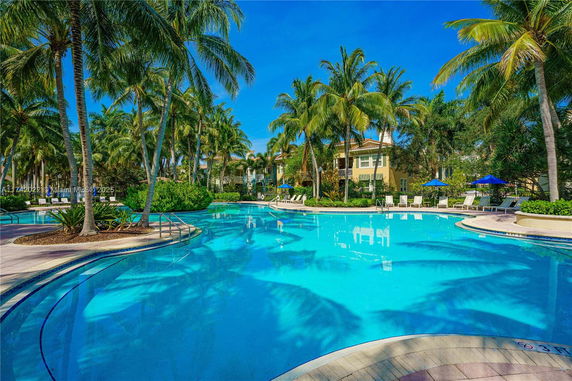 Outdoor swimming pool surrounded by palm trees and residential buildings.
