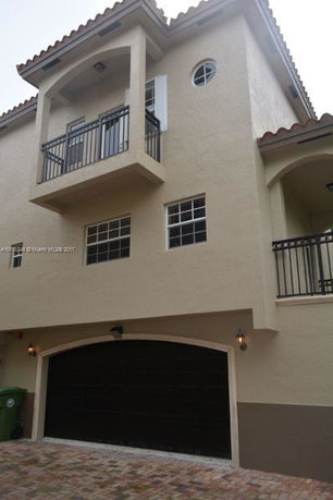 Front view of a multi-story house with a balcony and an arched garage door.