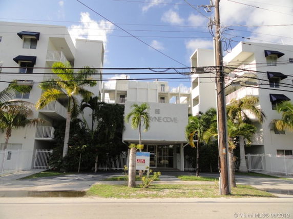 Front view of a multi-story residential building with balconies and palm trees.