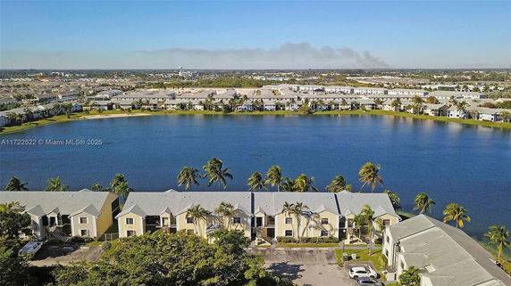 Overhead view of residential buildings near a lake surrounded by palm trees.