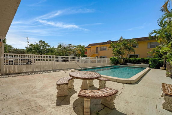 Outdoor swimming pool area with a decorative stone table and benches surrounded by fencing.