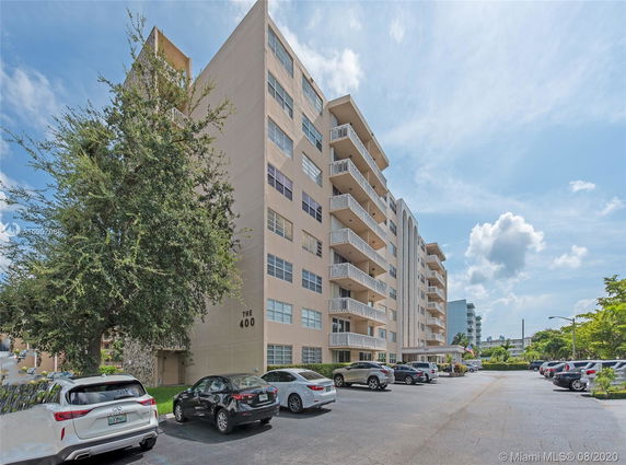 Front view of a multi-story residential building with balconies and parking area.