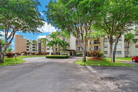 Front view of a multi-story residential building with balconies and surrounding greenery.