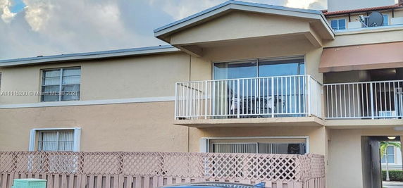 Front view of a two-story house with balconies and a fenced area.