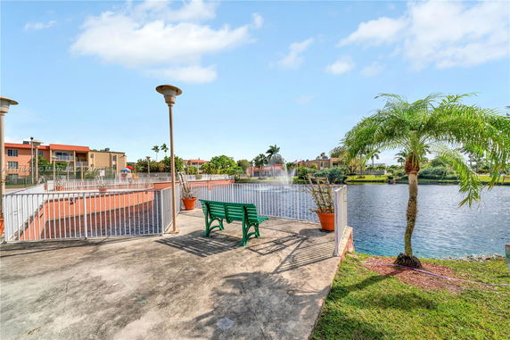 View of a waterfront area with benches, lampposts, and a fenced pathway overlooking a scenic body of water and nearby buildings.