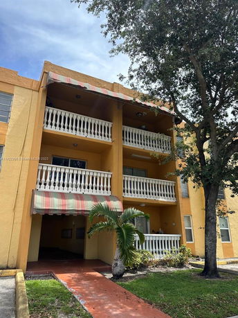 Front view of a three-story apartment building with balconies and an entrance shaded by an awning.