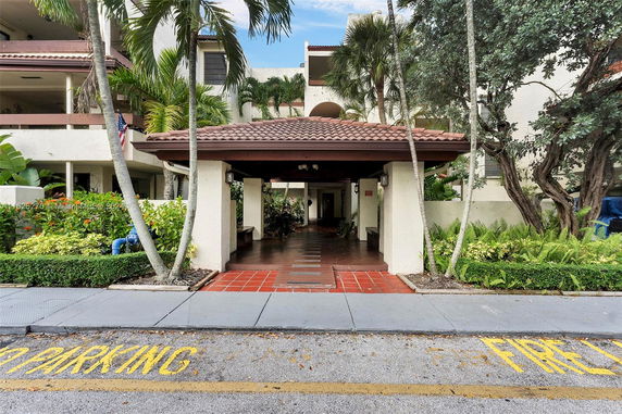 Front view of a building with a covered entrance and tropical landscaping.