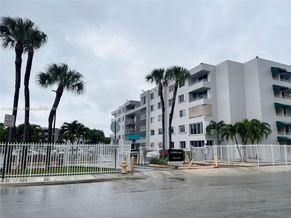Front view of a multi-story apartment building with balconies and surrounding palm trees.