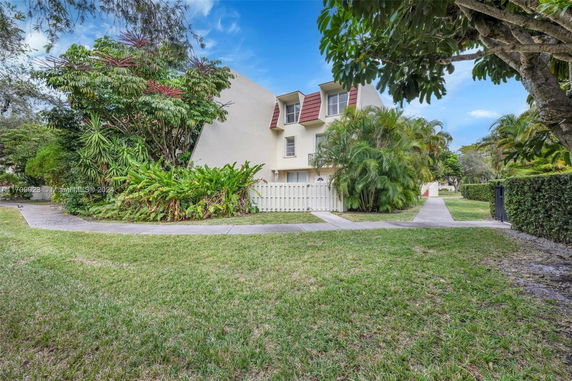 Front view of a two-story house with a white fence and lush greenery.