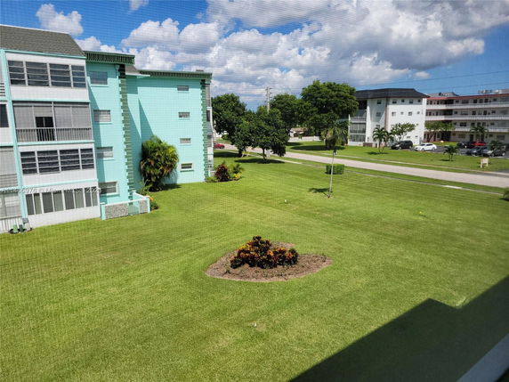 View of surrounding area showing a light blue building with multiple floors, windows, and a grass lawn.