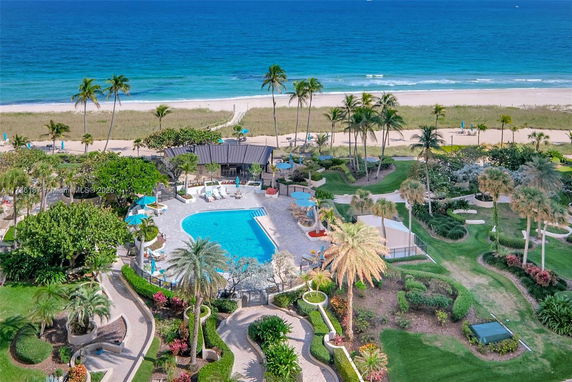 Aerial view of an outdoor swimming pool area with surrounding gardens and pathways near the beach.